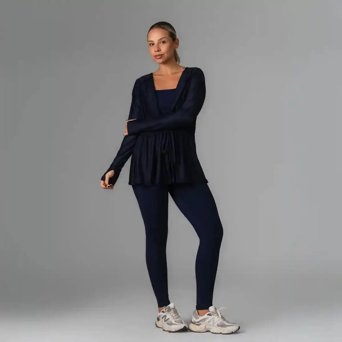 Casaco Grazi dry fit fluido com amarração na cintura, azul-marinho, por cima de top e legging.